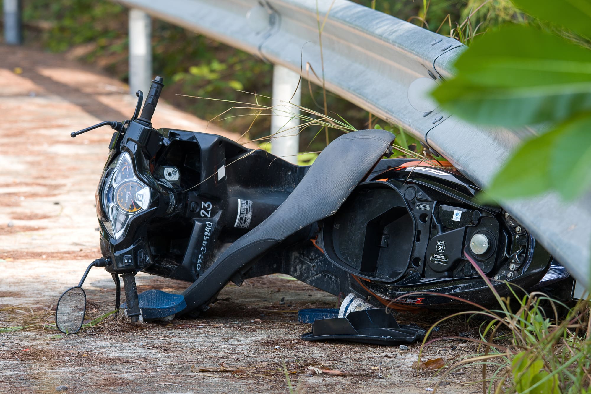 A wrecked motorcycle laid on its side under a roadside guard rail.